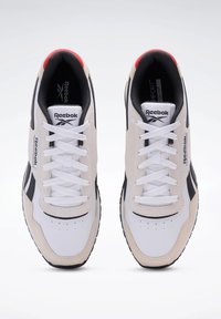 Weiße und beige Sportschuhe mit schwarzen Akzenten, synthetisches Obermaterial, runde Zehenpartie, Schnürung und strukturierten Gummisohlen.