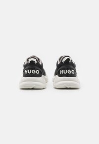 Sneaker nere con una finitura testurizzata e suole bianche. Sul retro è presente "HUGO" in lettere bianche in grassetto per il marchio.