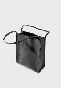 Sac cabas en cuir verni noir avec un design structuré, ouverture supérieure et deux longues anses pour le transport. Texture lisse et style minimaliste.