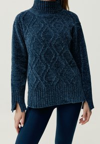 Mörkblå stickad tröja med hög krage, texturerat diamantmönster och ribbad fåll. Sidossprund ökar komfort och passform.