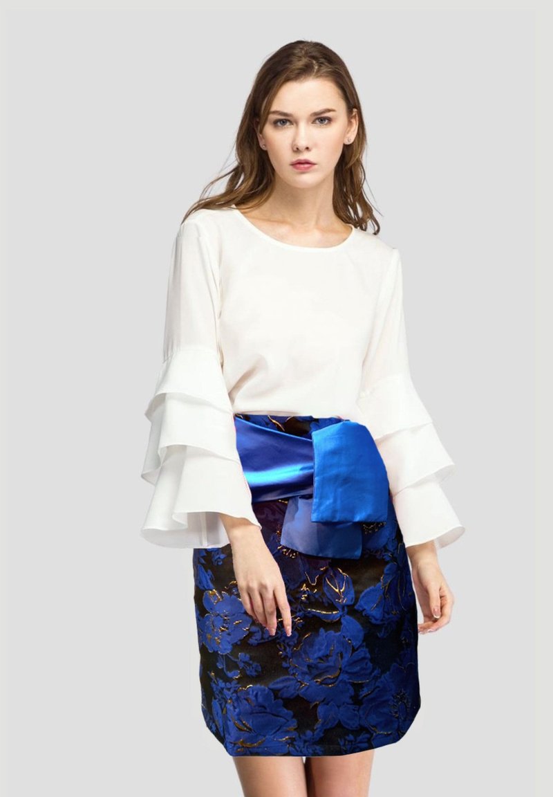 Blusa blanca de manga larga con puños con volantes, combinada con una falda azul de estampado floral con un cinturón azul sólido en la cintura.