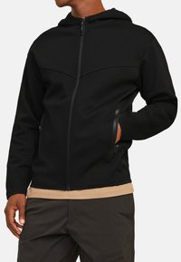 Zwarte zip-up hoodie met een capuchon, voorzien van een gladde textuur, een getailleerd ontwerp en twee zijzakken met verborgen ritsen.