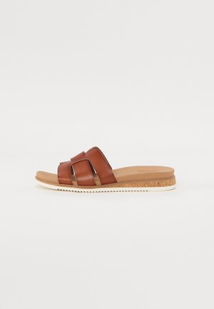 Brun læder slidesandal med brede stropper, korktekstureret mellemsål og hvid riflet sål på en neutral baggrund.