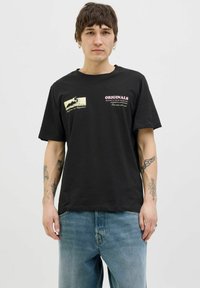 Zwarte katoenen t-shirt met grafische prints aan de voorkant in witte en roze tekst. Korte mouwen en een relaxte pasvorm, gecombineerd met lichtblauwe denim jeans.
