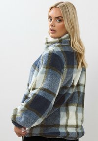 Rutig fleecejacka i blått, vitt och olivgrönt med hög krage och avslappnad passform, med en mjuk textur och överdimensionerade ärmar.