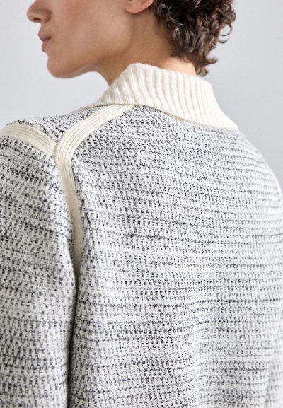 Strikket sweater i grå og crema med et struktureret mønster. Har en ribbet hvid krave og skulderdetaljer i en lysere nuance.