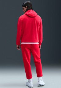 Rode sweatshirt en bijpassende trainingsbroek van zachte stof, met een capuchon en geribbelde manchetten, gecombineerd met witte sportschoenen.