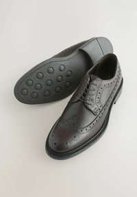 Des richelieus en cuir marron foncé présentent un dessus texturé, des détails perforés et une semelle en caoutchouc avec des motifs de traction circulaires.