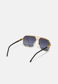 Ochelari de soare cu ramă metalică aurie, lentile octogonale, lentile cu gradient gri închis și brațe negre cu textură, dotate cu mânere texturate și accente metalice.