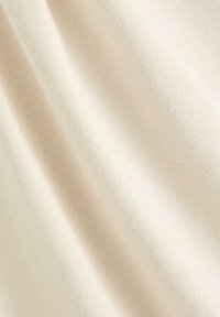 Kremfarvet, blødt stof med en glat, let tekstureret overflade, synligt fint strikkemønster og blid fald.