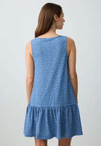 Abito senza maniche blu con motivo a pois, orlo arricciato e corpino aderente; realizzato in tessuto leggero con una texture morbida.