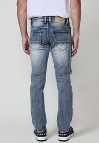 Vaqueros de mezclilla azul claro con corte ajustado, detalles de desgaste, diseño de cinco bolsillos y costuras en contraste. Usados con zapatillas negras.