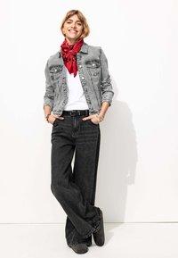 Veste en denim grise sur une chemise blanche, associée à un jean noir à jambes larges et un bandana rouge. Look élégant et décontracté avec des accessoires superposés.