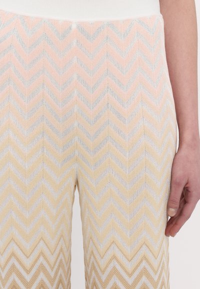 Pantalons en tricot à motifs en chevrons dans des teintes pastel de rose, jaune et argent. Présentent une finition texturée avec des largeurs de rayures variées et des coutures horizontales.