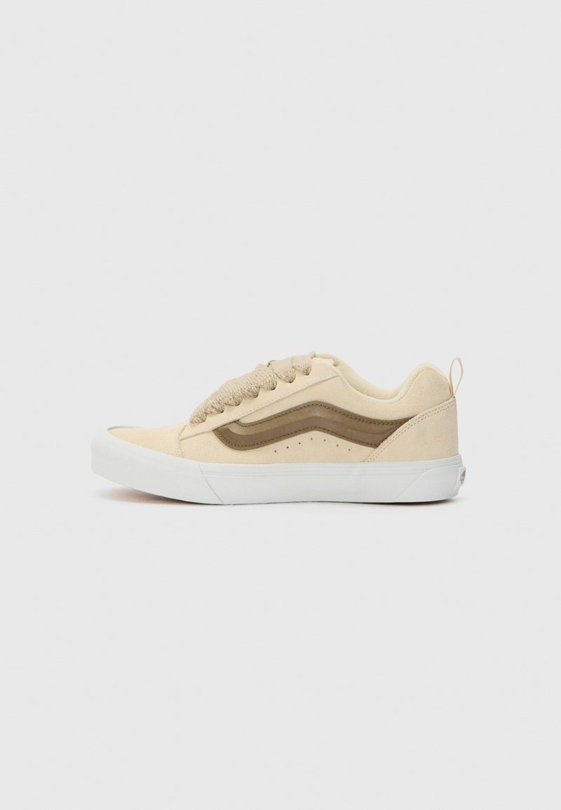 Shoe made of beige suede with brown accents, featuring a classic lace-up design, rounded toe, textured upper, and white rubber sole.