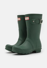 Botas de goma verdes impermeables con un acabado mate, puntera redonda y un acento decorativo de hebilla. Suelas resistentes con relieves texturizados para el agarre.