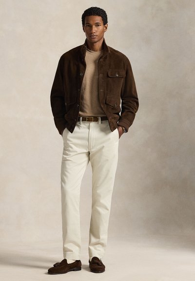 Rudos spalvos zomšinė striukė, rudas megztinis, smėlio spalvos kelnės ir rudi bateliai. Pastebimos detalės – priekinės kišenės ir diržas su metaline sagtimi.