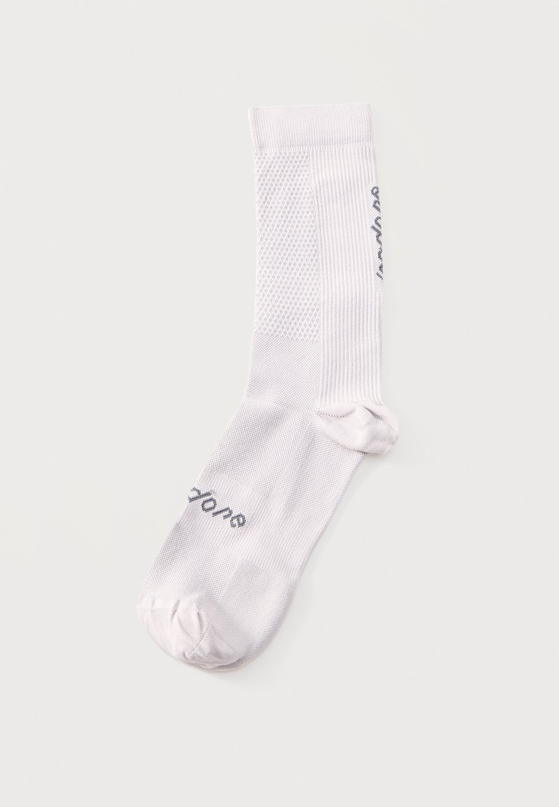 Μονή λευκή κάλτσα μέχρι τη μέση της γάμπας με υφασμένους υφή πίνακες και μαύρο κείμενο κοντά στα δάχτυλα και κατά μήκος της πλευράς, τοποθετημένη επίπεδα σε ανοιχτό φόντο.