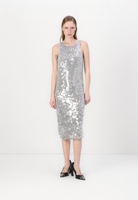 Vestido prateado com lantejoulas, design sem mangas, corte até ao joelho e ajuste reto. Combinado com saltos pretos em patente.