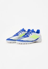 Blauwe en witte voetbalschoenen hebben groene accenten, een slank ontwerp met een geprofileerd oppervlak en prominente veters voor een veilige pasvorm.