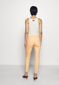 Fitted white tank top and peach chinos, showcasing a smooth texture. The tank has a small brand label; pants feature back pockets and sleek design.