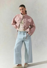 Veste oversized rose clair, top blanc à motifs, jeans larges bleu clair et chaussures tissées beiges. Textures simples et coupe décontractée.