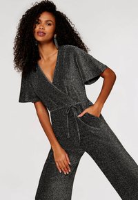 Zwart glinsterende jumpsuit met korte mouwen, V-hals, strikceintuur en zijzakken; gemaakt van een gestructureerde, metallic stof.