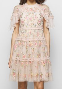Robe brodée de fleurs en tissu rose transparent. Comprend des manches à volants et une jupe en tulle superposée avec des motifs floraux éparpillés.