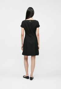 Μαύρο �φόρεμα κοντό μανίκι με εφαρμοστό μπούστο και φούστα που φουσκώνει, διαθέτει λεπτομέρεια με κουμπί στον πίσω λαιμό. Ομαλή υφή υφάσματος.