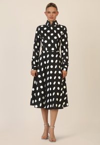 Schwarzes Kleid mit weißen Punkten, mit einem Kragen, langen Ärmeln und einem ausgestellten Rock. Glattes Material, knielanges Design, elegante Silhouette.