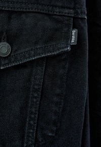 Svart denimjacka med knappstängning, bröstficka med lock och en liten märkesetikett. Slät textur med en klassisk design.