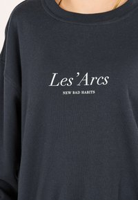 Mörkblå sweatshirt med avslappnad passform. Har texten "Les'Arcs NEW BAD HABITS" i vit tryck. Mjukt tyg, ribbat nackparti.