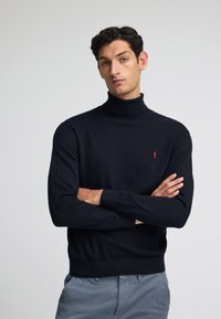 Maglione a collo alto nero realizzato in un materiale a maglia fine. Presenta un piccolo logo rosso sul petto e polsini e orlo a costine.