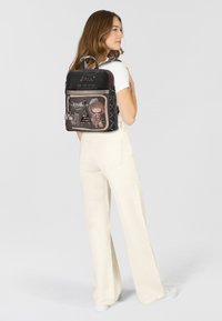 Schwarzer, gepolsterter Rucksack mit grafischem Design, das ein Mädchen mit einer Kamera und dem Eiffelturm zeigt. Weiches Material, doppelte Schultergurte und Reißverschluss.