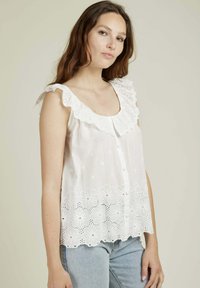 Haut sans manches blanc avec bordure en dentelle ajourée, broderie florale en bas et boutons à l'avant. Fabriqué à partir d'un tissu léger et respirant.