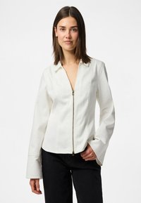 Camicia bianca con zip, colletto, maniche lunghe e polsini a campana. Tessuto liscio con cuciture visibili sul davanti.