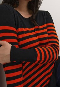 Pull rayé noir et orange avec un col rond et des manches longues, doté de poignets côtelés et d'une texture douce.