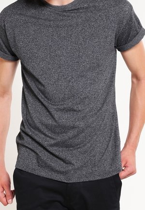 Man wearing a short-sleeve, dark gray, heathered t-shirt and black pants, standing against a plain background.