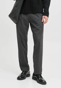 Grau zugeschnittene Hose mit geradem Schnitt, aus glattem Stoff gefertigt. Getragen mit einem schwarzen gerippten Pullover und glänzenden schwarzen Schuhen.