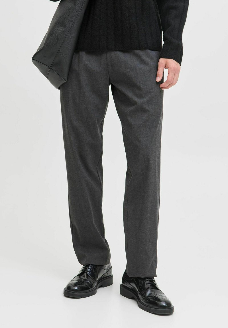 Grau zugeschnittene Hose mit geradem Schnitt, aus glattem Stoff gefertigt. Getragen mit einem schwarzen gerippten Pullover und glänzenden schwarzen Schuhen.