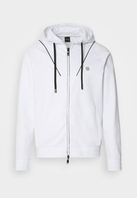 Haut à zip blanc avec des accents noirs, cordons ajustables et un petit logo sur la poitrine. Fabriqué en tissu doux et lisse.