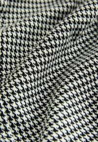 Kanga, millel musta ja valge houndstooth mustriga, millel on pehme ja tekstuuriga pind. Kangas on tihedalt kudunud, luues eristuva disaini.
