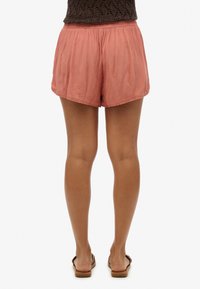 Pantalones cortos de tela ligera en color melocotón con una cintura elástica y dobladillo con ondas. La textura parece suave, con un corte relajado.