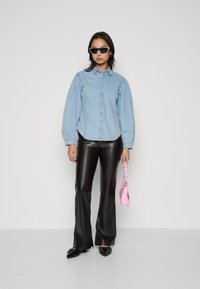 Lyseblå denimskjorte med pufsermer, parret med svarte faux skinn flared bukser. Holder en liten rosa håndveske. Svarte solbriller.
