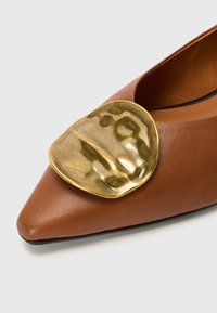 Brown leather pointed-toe shoe with a prominent gold-toned metallic accent on the upper, featuring a textured surface and smooth finish.