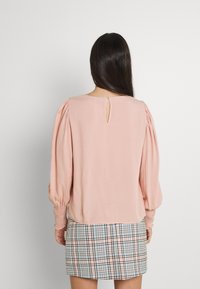 Blusa rosa con mangas abullonadas y detalle de ojal en la parte posterior, combinada con una falda de cuadros con un patrón multicolor. Textura suave, diseño casual.