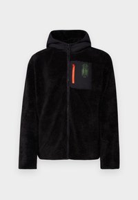 Giacca a zip nera in pile con cappuccio, dotata di tasca sul petto in tessuto nero con zip arancione e dettagli grafici verdi.