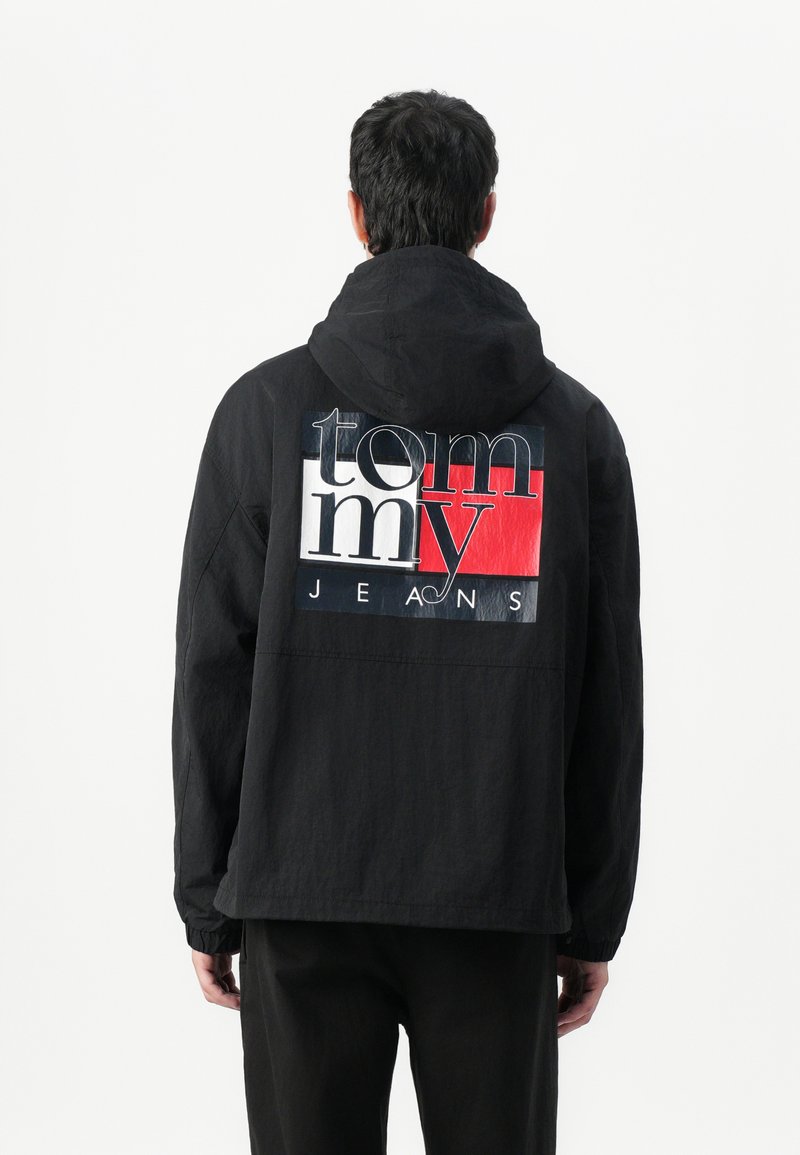 Zwarte hoodie met een gestructureerde afwerking, voorzien van een gedurfde logoprint in wit en rood over de achterkant. Elastische manchetten maken de look compleet.