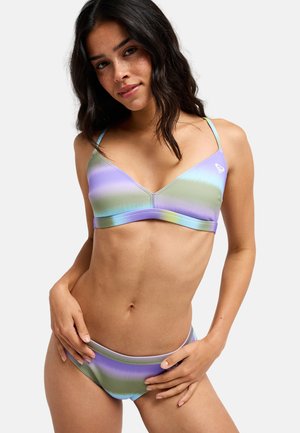 Kobieta o ciemnych, falowanych włosach, ubrana w pastelowy fioletowo-zielono-niebieski bikini z cienkimi ramiączkami, pozująca z rękami przy biodrach.