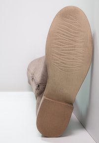 Bottine en daim de couleur beige avec une semelle en caoutchouc texturée et nervurée. Elle possède une fermeture éclair latérale et une tige en tissu lisse. Taille indiquée : 38.